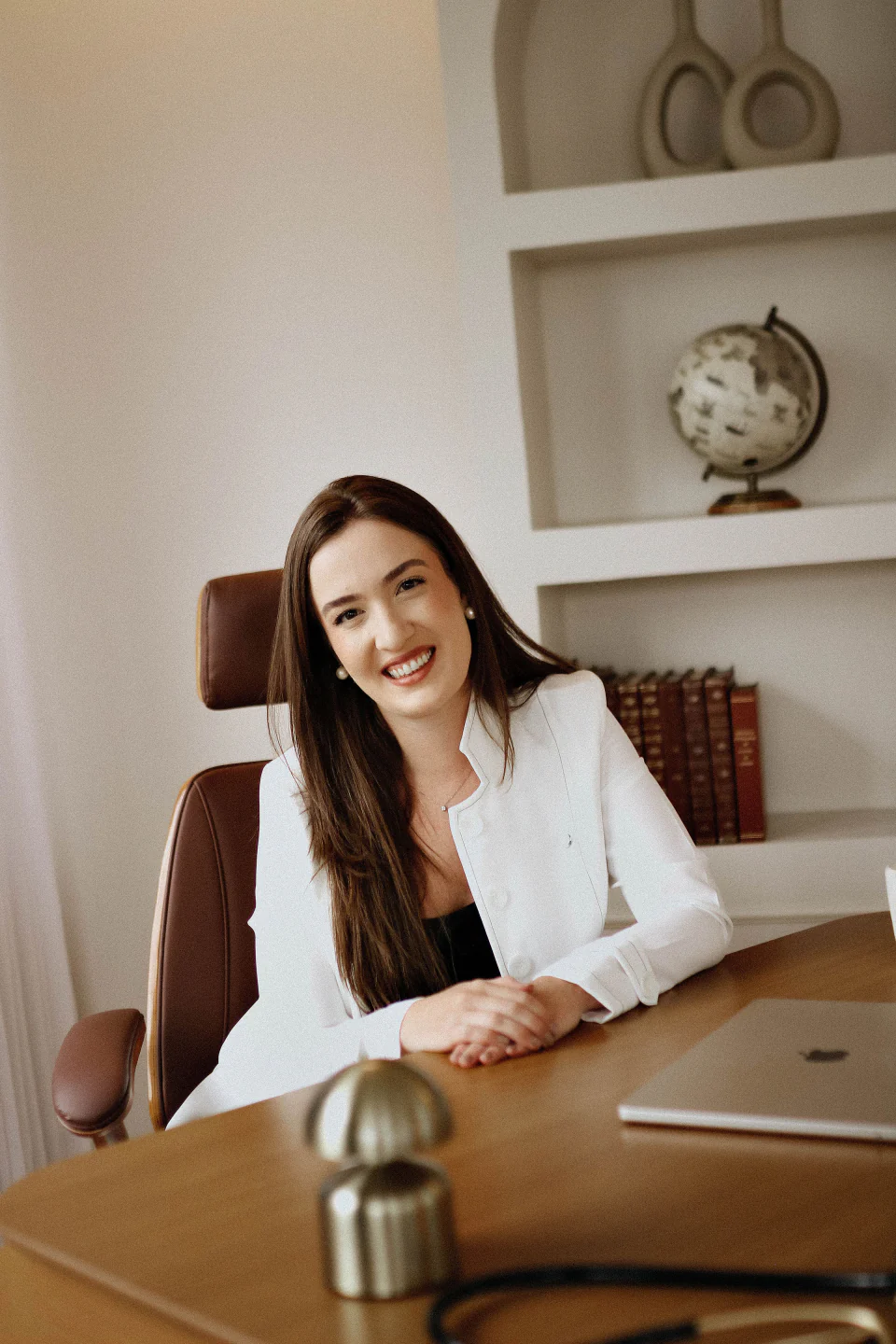Dra. Danielle Guazzelli sorrindo à mesa, com blazer branco