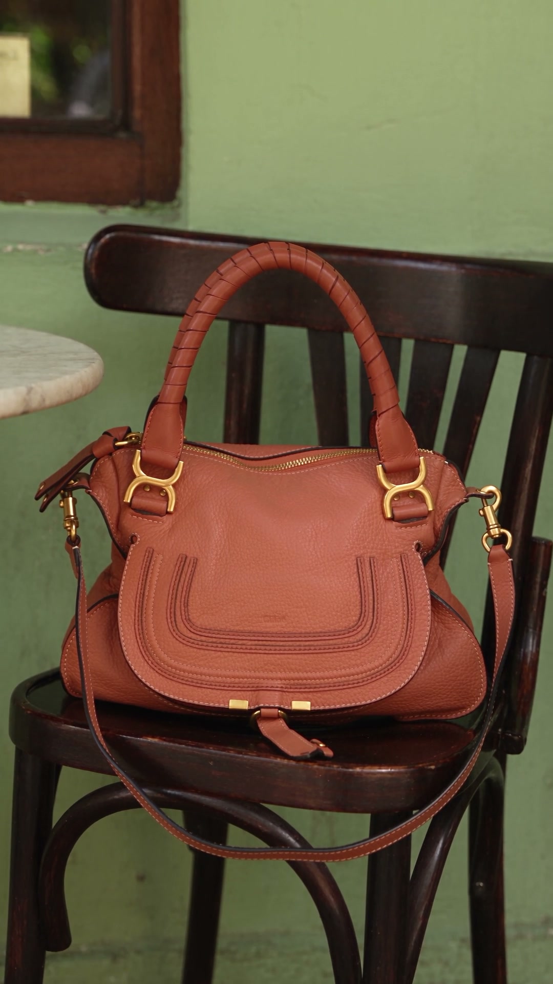 Fotograma do vídeo: bolsa apoiada em uma cadeira no café, com a frente visível.