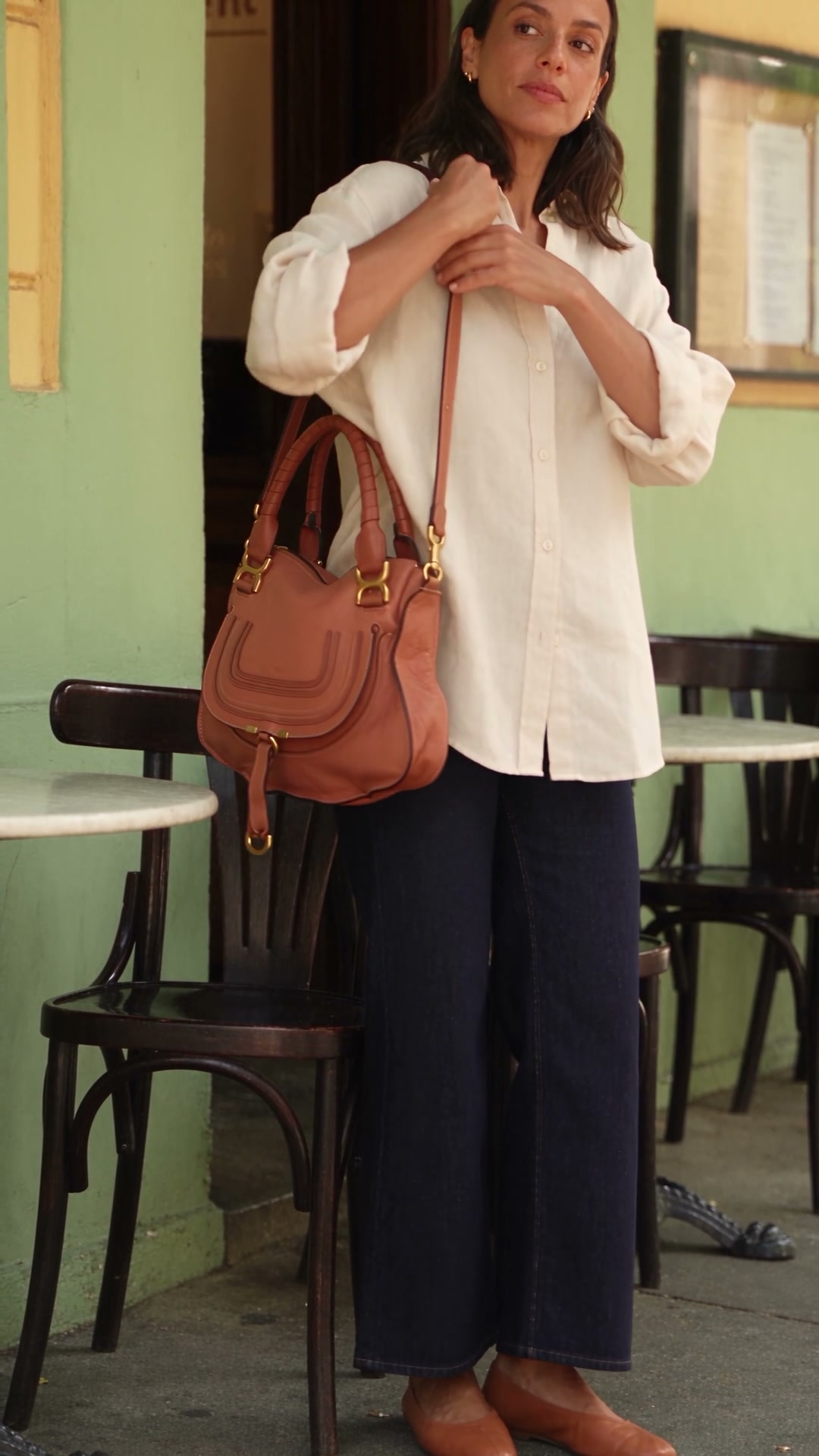 Fotograma do vídeo: mulher de camisa clara com a bolsa no ombro, ao lado do quadril.