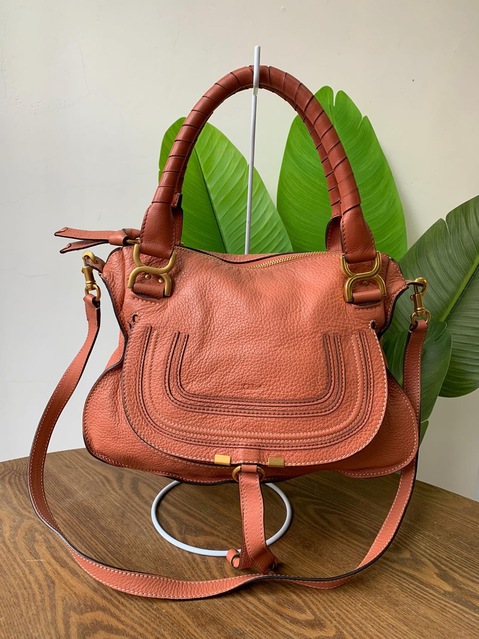Foto real da bolsa terracota, de frente, com duas alças curtas, uma alça longa e ferragens douradas.